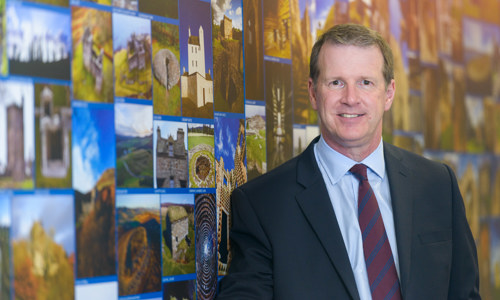 Alex Paterson wearing a suit, standing next to a wall covered in images